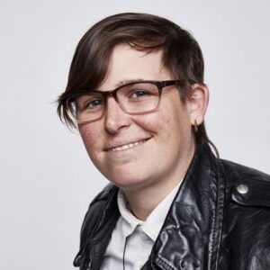 Image of a gender-neutral person with glasses wearing a leather jacket and smiling