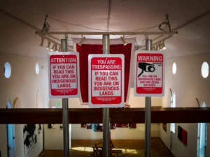 A red and white sign reads YOU ARE TRESPASSING If You Can Read This You Are on Indigenous Land
