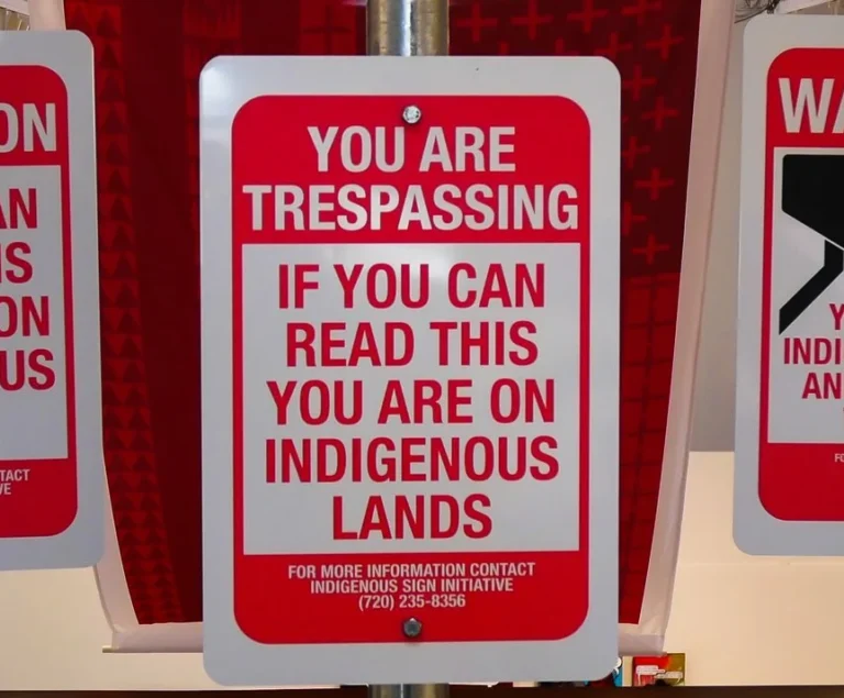 A red and white sign reads YOU ARE TRESPASSING If You Can Read This You Are on Indigenous Land