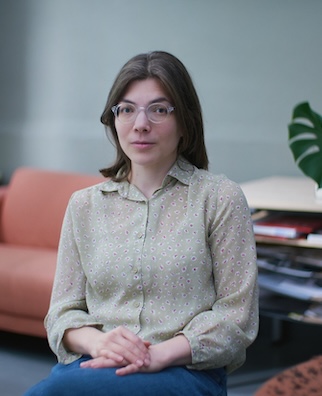 A white woman with shoulder-length brown hair wearing a light green shirt sits with hands folded.