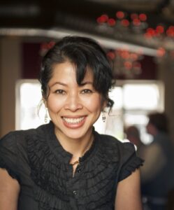An asian woman wearing a black shirt with her hair up smiles at the camera