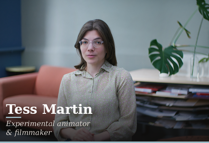 Portrait of Tess Martin, experimental animator and filmmaker, seated indoors with a plant and shelves in the background.