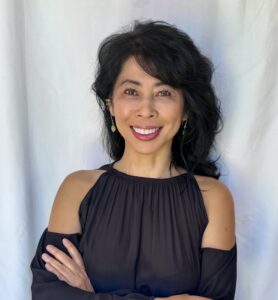An Asian woman wearing a black dress stands smiling with arms folded in front of a white backdrop. Loung Ung, author of First They Killed My Father: A Daughter of Cambodia Remembers.